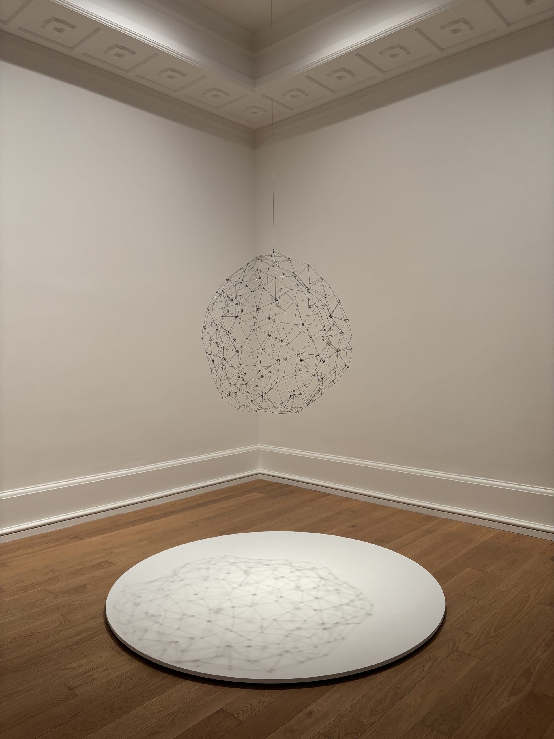 Escultura esférica de alambre suspendida sobre una peana blanca en una sala del museo.
